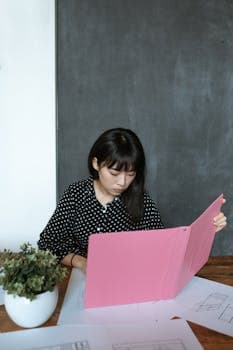 Awomaninablackandwhiteshirtislookingatapinkbook.