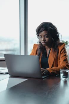 Focused female entrepreneur working on laptop in a modern office environment.