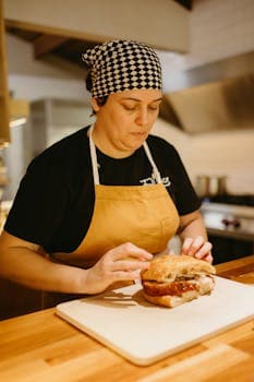 A woman chef focuses on preparing a delicious sandwich in a professional kitchen setting.