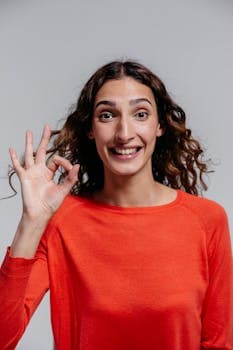 A happy woman in a red sweater smiling and making an OK gesture in a studio setting.