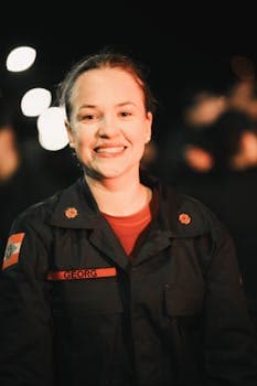 A smiling woman in uniform at a night event with blurred lights in the background.