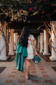 Graduate walking down a scenic walkway in Tampa, holding a cap with gown over shoulder.
