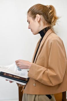 Brunette woman in brown coat reading a law book indoors.