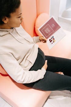 A pregnant woman sits comfortably indoors reading a brochure, symbolizing information gathering during pregnancy.