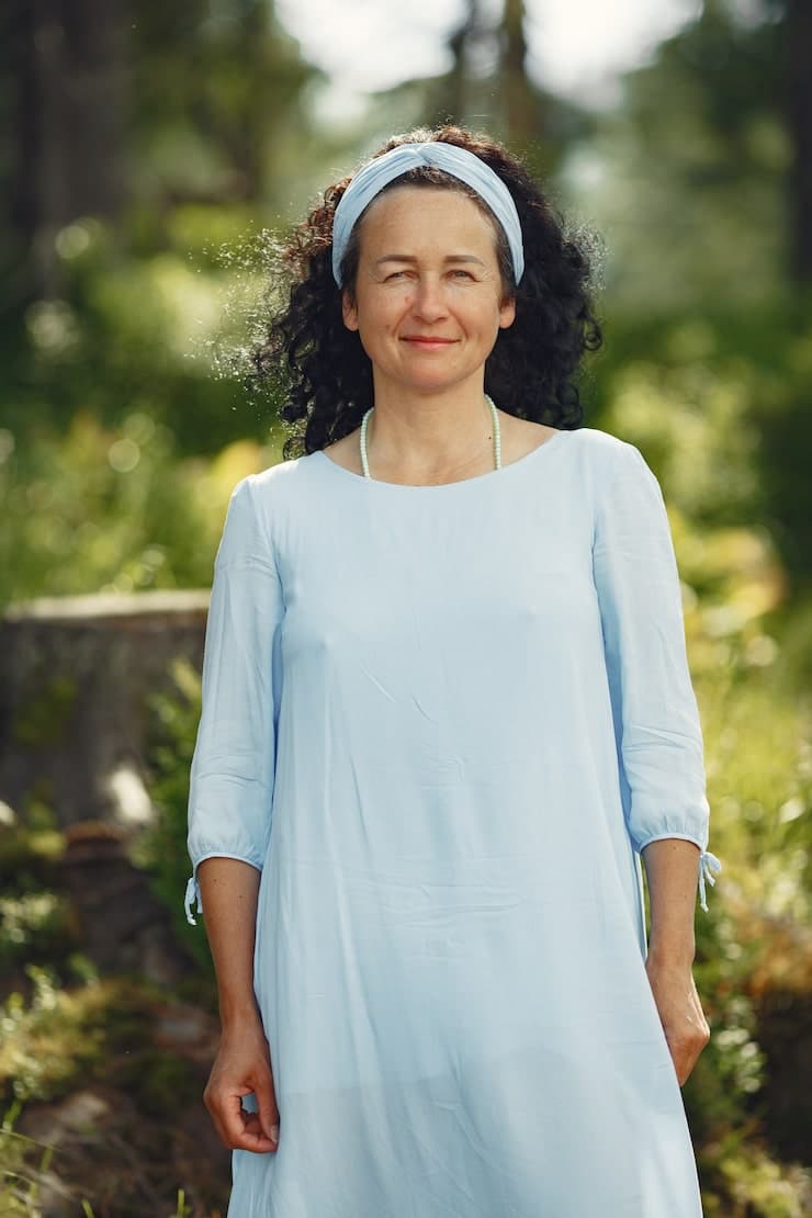 A woman wearing a blue dress is standing in a forest. She is smiling ...