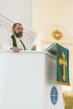 Pastor in white robe delivers sermon from church pulpit with a cross banner.