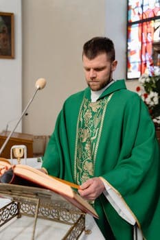 A priest in a green stole reads from a book during a church ceremony.