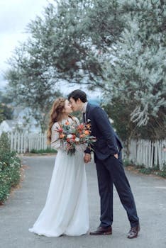 A romantic scene of a couple kissing at their outdoor wedding ceremony, holding a vibrant bouquet.