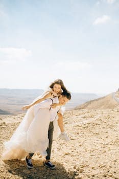 A couple enjoying a playful moment during their wedding photoshoot in a stunning desert landscape.