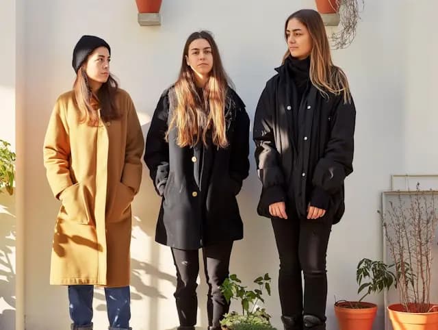 Three women are standing together in front of a white building, wearing ...